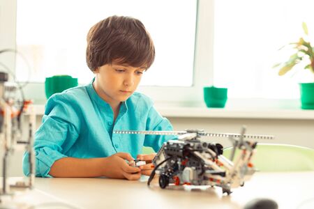 Trying to set in motion. Concentrated elementary schoolboy sitting in the classroom with remote...