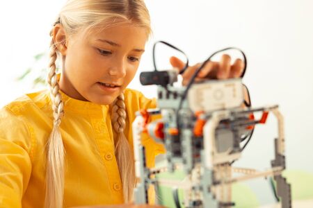 Exciting things. Focused elementary schoolgirl playing with complicated robot she made using construction set.の写真素材