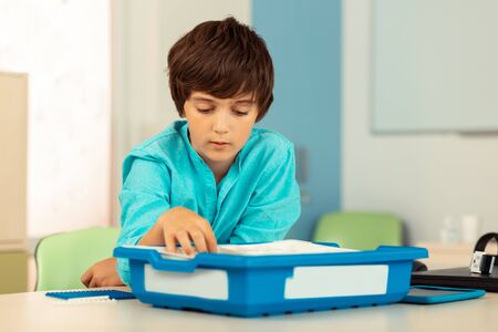 Choosing materials. Thoughtful boy sitting in the classroom and looking for details in construction...