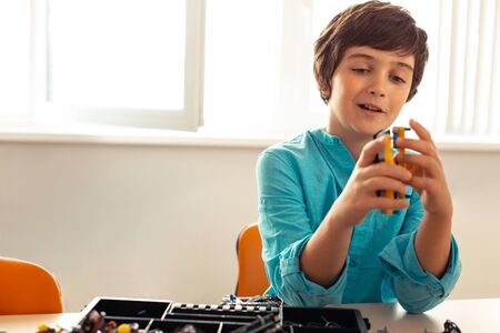 Making new construction. Enthusiastic smiling pupil sitting in the classroom with a box full of...