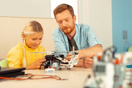 Learning to create. Attentive teacher and interested pupil sitting together at the desk during the lesson building a helicopter together.の写真素材