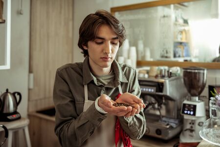 Gorgeous young man holding coffee beans in hands and smelling