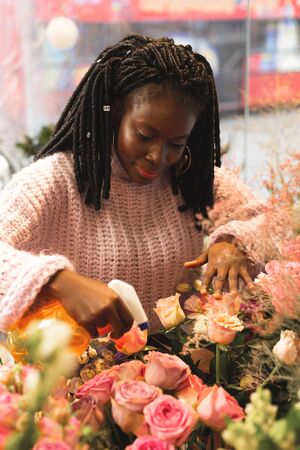 My workplace. Cheerful dark-skinned woman bowing head while watering bouquet