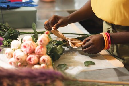 Kind international woman standing at the desk and tying a bow on flowersの写真素材