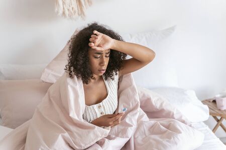 Attentive young female touching her forehead while measuring temperatureの写真素材