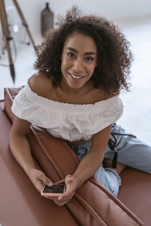 Cheerful female sitting on the sofa with a smartphone in her hands