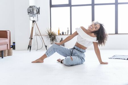 Pretty young lady smiling sitting on the floor leaning on her handの写真素材