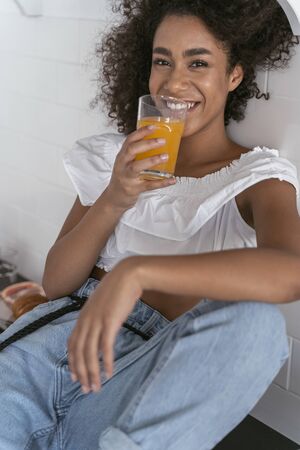 Beautiful woman sitting on the countertop wit a glass of juice near her mouth