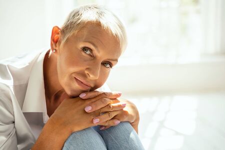 Pleased blonde leaning hands on knees while posing on cameraの写真素材