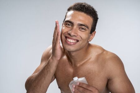 Handsome young man raising his hand spreading aftershave on his faceの写真素材