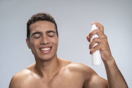 Cheerful young male closing his eyes spraing water on his faceの写真素材