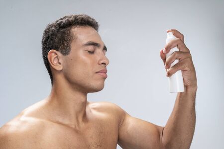 Good-looking man spraying his face with eyes closedの写真素材