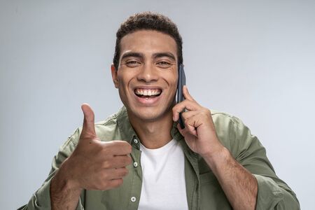 Handsome young male talking on the phone and giving a thumbs-upの写真素材