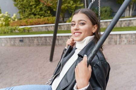 Beautiful young woman sitting on a swing and smiling