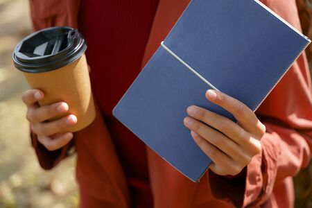 Close up picture of a hands of young woman holding a cup of coffee and a notebook