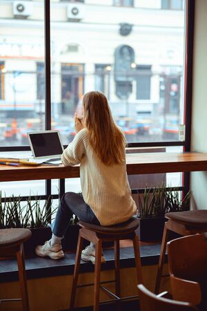Back view of a young woman sitting on a stool in a cafe