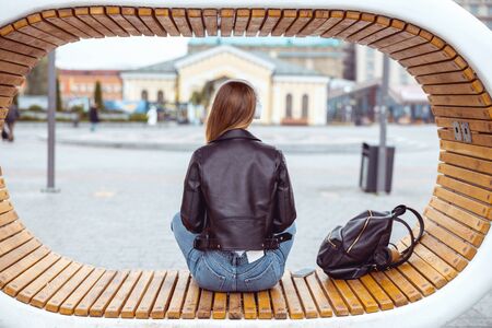Back view of a female sitting in the middle of an eco-benchの写真素材
