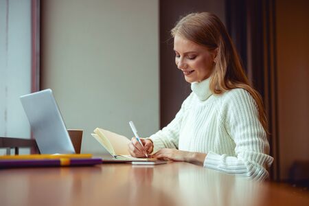 Positive young female writing in her notebook at the desk