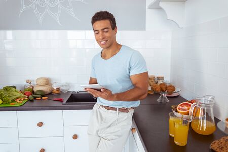 Pleased male keeping smile on his face while staring at his gadget