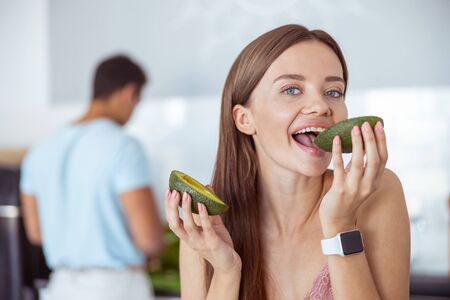 So tasty. Charming girl being on the foreground while biting green avocadoの写真素材