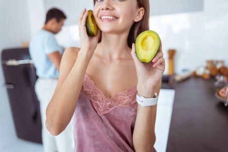 Positive delighted brunette girl holding avocado in both hands
