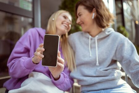 Keep smiling. Cheerful young woman holding smartphone in both hands while taking picture