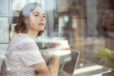 Young woman looking at big window while being deep in her thoughts