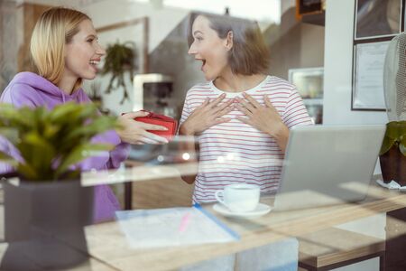 In shock. Pleased girl holding present in both hands while having festive mood after classesの写真素材