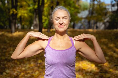Pleasant mature fit lady doing elbow circles outside