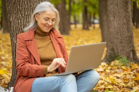 Smiling woman writing a message on her laptop outside
