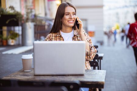 Beautiful young woman talking on the phone sitting in the street coffee shopの写真素材
