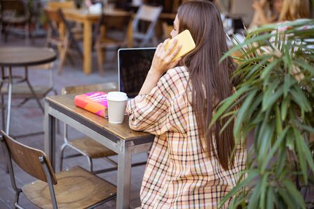 Back view on a good-looking young female sitting at the street cafe during her working dayの写真素材