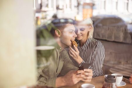 Handsome young man biting a biscuit his beautiful girlfriend giving to himの写真素材