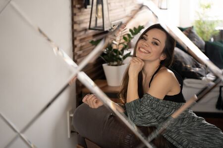 Happy woman in room with modern interior looking at herself in mirror