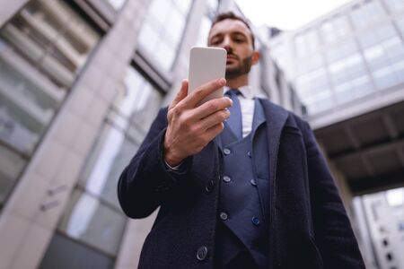 Just attention. Serious bearded male person standing near modern buildings while staring at his...