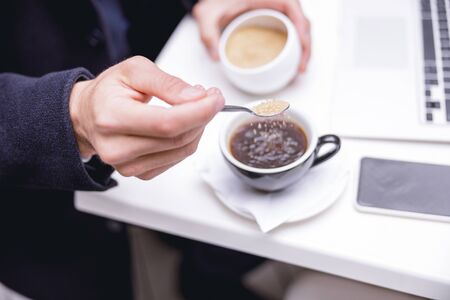 Relaxed office worker adding sugar into coffee while spending his break in cafeの写真素材