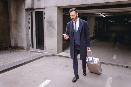 Waiting for taxi. Kind male person wheeling his luggage while going from parkingの写真素材