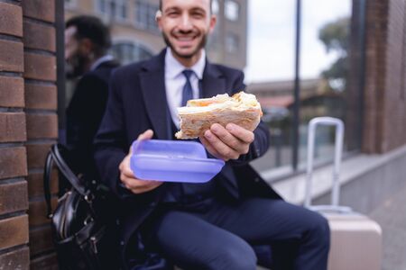 Take it. Cheerful bearded male keeping smile on his face while going to eat sandwichの写真素材