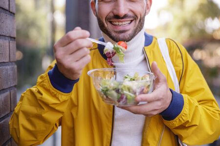 Healthy food. Handsome brunette male person holding box with salad while having lunch outsideの写真素材