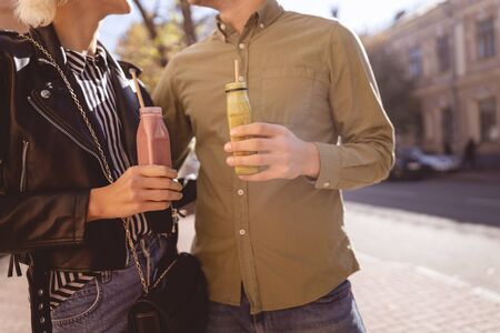 Handsome man and pretty woman standing together on the street and holding smoothiesの写真素材