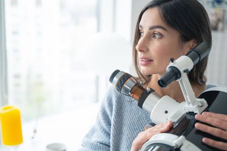 Beautiful young woman looking away and putting hands on a telescope