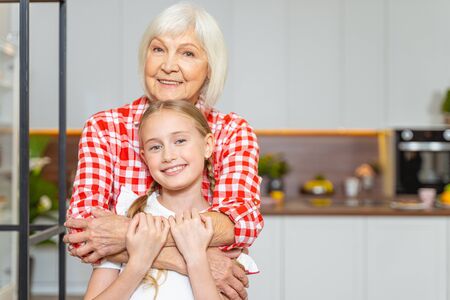 Merry aged woman clasping her smiling grandchild in her arms