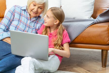 Aged woman sitting with her grandchild on the carpetの写真素材