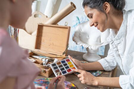 Pretty adult lady looking at paints with a small kid in art room. Art concept