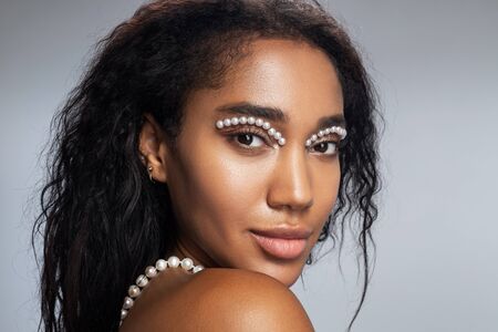 Charming Afro American lady wearing jewelry with pearls against light background. Beauty and jewelry conceptの写真素材