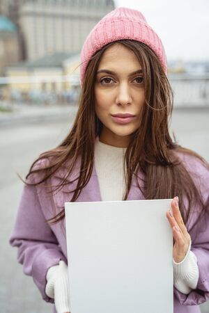 Attractive brunette holding white sheet of paper in both hands while attracting attentionの写真素材