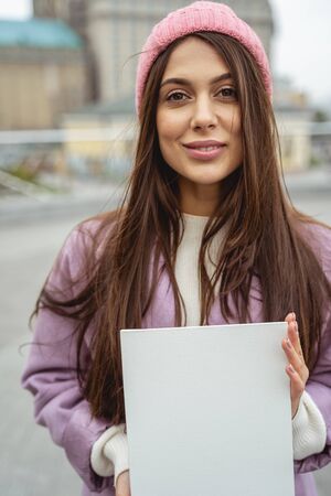 Pleased girl keeping smile on her face while demonstrating blank paper sheet