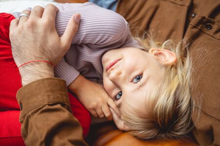 Cute child resting on couch while father holding her in his arms stock photoの写真素材