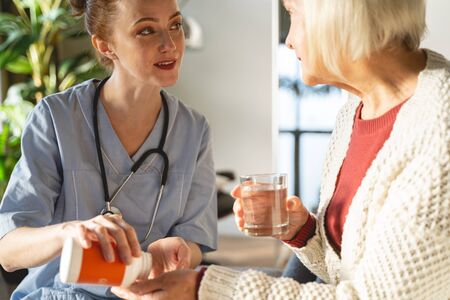 Pleased senior female sitting in semi position and looking at her practitionerの写真素材