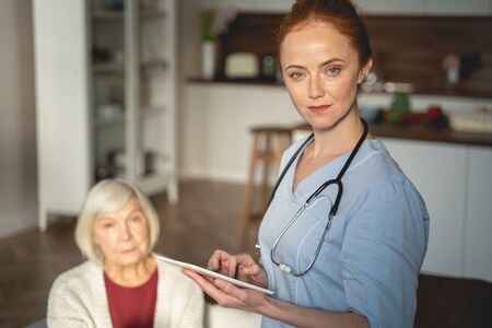 Kind woman wearing medical uniform, holding tablet in her handsの写真素材